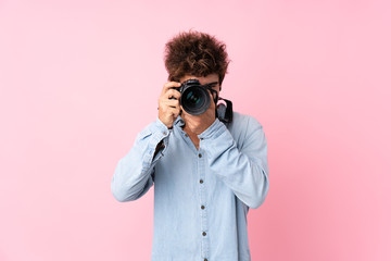 Young caucasian man over isolated pink background with a professional camera