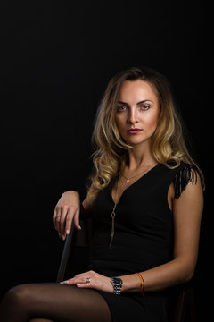 A delightful young woman with long blonde hair in a small black dress with no sleeves