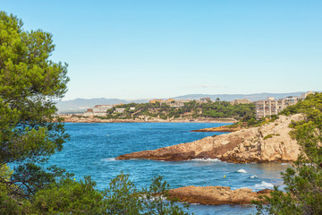 Fototapeta na wymiar Seascape: blue sea with rocky shores and green trees. Spain, Costa Dorada, Salou