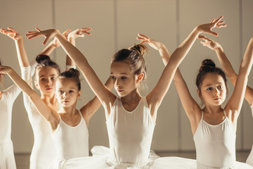 Young happy caucasian little ballerinas, awesome ballet dancers practicing some dance element in a...