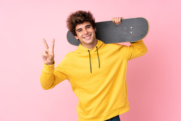 Young caucasian man over isolated pink background with skate and making victory gesture © luismolinero