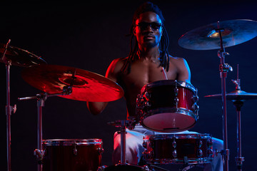 good-looking artistic african black male drummer enjoying playing drums over dark background