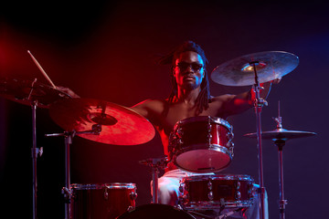 artistic african black male drummer enjoying playing drums over dark background