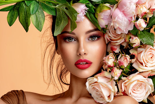 Beautiful white girl with flowers. Stunning brunette girl with big bouquet flowers of roses. Closeup face of young beautiful woman with a healthy clean skin. Pretty woman with bright makeup