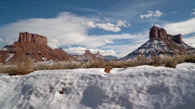 Timelapse of buttes in Castle Valley Utah during winter on sunny day as clouds move through the sky and snow covers the landscape moving on slider viewing Castleton Tower and Parriot Mesa.