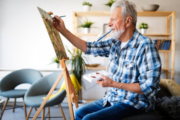 Handsome mature man artist paints on canvas painting on the easel