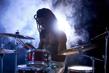 african young naked handsome man hitting on drums, perussion instruments isolated over smoky background. sit with head down