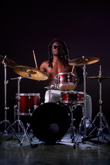 Fototapeta premium Portrait of african man playing on drums and cymbals, wearing eyeglasses and holding sticks. isolated over dark background