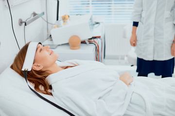 Obraz premium calm patient lying on bed and looking up with medical frontlet, wearing white bathrobe