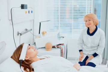 Fototapeta premium careful nurse or doctor is always near her patient lying on bed, isolated in white hospital room. wearing white doctor's uniform, bathrobe. using special medical equipment, devices