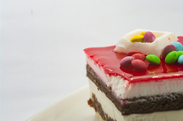 closeuo of a Big piece of cake in a white plate with multi-colored candies on it