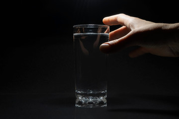 Glass of water and hand closeup on black.