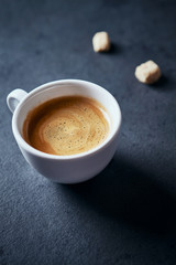 Cup of coffee and two brown sugar cubes on dark stone background. Close up.