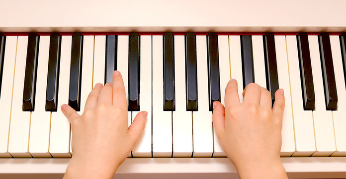 The child's hands play on the piano keys