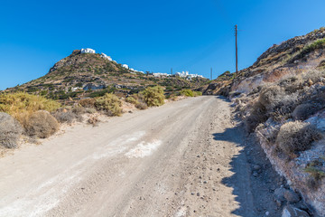 Dirty road with rocks and vegetation and Plaka village in background