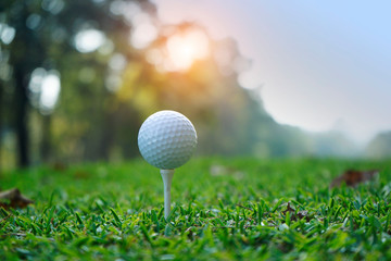 Golf ball on tee in beautiful golf course at sunset background.