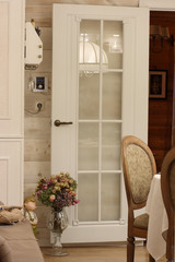 A bouquet of dried flowers in a vase against a white door with reflection of a lampshade in a living room