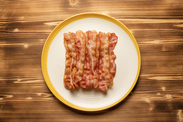Top view of many slices of fried bacon on a plate with wooden surface background 