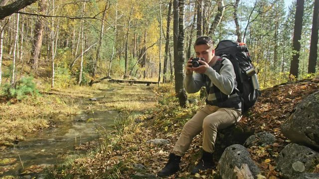 Traveler photographing scenic views in forest by mountain river. Man shooting picturesque views. The guy takes photo and video on dslr camera. Professional photographer traveler.
