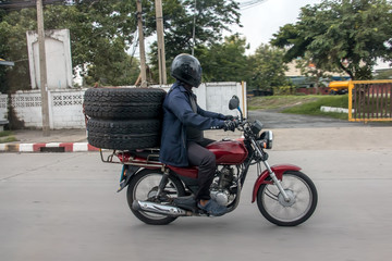 Obraz na płótnie Canvas Transporting tires on a motorcycle. Man carries big tire on motorbike, Thailand.