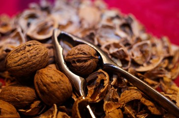 Close up pile with cracked walnut shells and isolated retro lever nutcracker with red background.