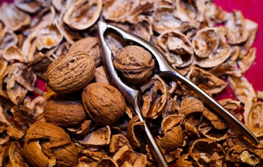 Close up pile with cracked walnut shells and isolated retro lever nutcracker with red background.