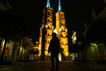 Wroclaw. Silhouette of a traveller man with backpack in front of illuminated cathedral of St. John the Baptist on Ostrow Tumski