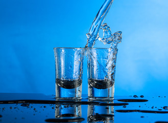 two falling glasses with vodka in motion are frozen with a spray and a splash