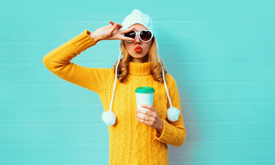Winter portrait young woman with coffee cup showing peace gesture wearing yellow knitted sweater,...