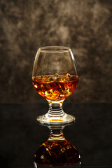Whiskey with ice or brandy in a glass on a glass reflective surface. Whiskey with ice in a glass. Whiskey or brandy. Selective focus.