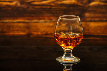 Whiskey with ice or brandy in a glass on a glass reflective surface. Whiskey with ice in a glass. Whiskey or brandy. Selective focus.
