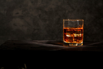 Whiskey with ice or brandy in a glass with lemon on a background of gray concrete on an old wooden table. Whiskey with ice in a glass. Whiskey or brandy. Selective focus.