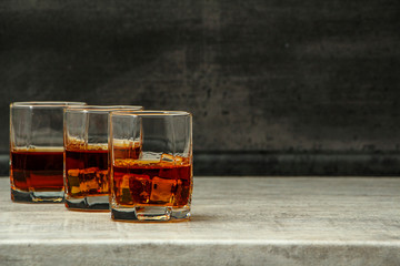 Whiskey with ice or brandy in a glass with lemon on a background of gray concrete on an old wooden table. Whiskey with ice in a glass. Whiskey or brandy. Selective focus.