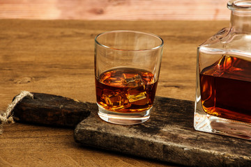 Whiskey with ice or brandy in a glass and a square carafe on an old wooden background. Whiskey with ice in a glass. Whiskey or cognac. Selective focus.