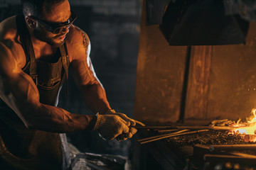 handsome muscular caucasian man with strong muscles on hands, side view on man opposite the fire, wearing eyeglasses for safety