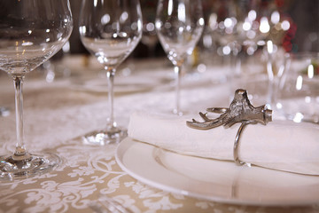 The white cloth napkin is secured with a ring in the form of a deer's head. Wine glasses are out of focus. Macro photo. Copy space.