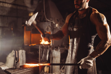 blacksmith beat hot metal with hammer isolated in dark workshop space, wearing leather brown apron and having muscular body