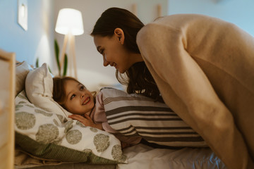 mom puts her daughter to bed and tells her something - 308272773