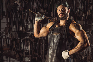 confident good-lloking artisan in leather brown apron or uniform, young caucasian forger with beard...