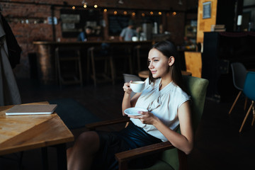 girl dressed in business clothes sits at a table in a cafe and drinks coffee