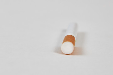 One cigarette lies with a filter to us on a white background