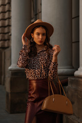 Outdoor fashion portrait of young elegant woman wearing hat, leopard print blouse, faux leather...