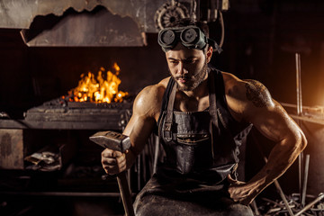 portrait of thoughtful muscular blacksmith holding hammer and looking down, wearing leather...