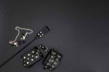Leather handcuffs, nipple clamps and stack for BDSM games on black background