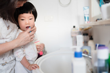 Obraz na płótnie Canvas Asian mother helping cute little toddler brushing her teeth, concept healthy happy child, health hygiene, kid oral hygiene, mother should help child brushing teeth, check up from birth to 6 years old.