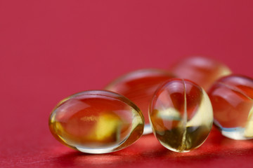 Medicinal background. Yellow omega 3 capsules on the right on a red background. Cropped shot, horizontal, close-up, free space. Medicine concept.