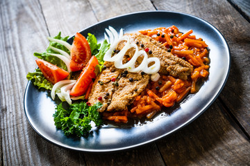 Fish dish - fried fish fillet on vegetable sauce on wooden table