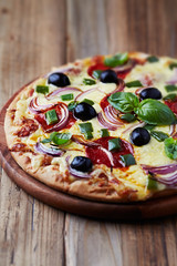 Pizza with salami, red onion, black olives and fresh basil. Rustic wooden background. 