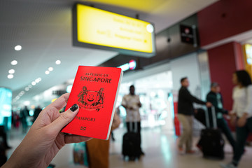 Close up of woman holding a Singapore passport over a blurred airport background. Digital composite.Japan and Singapore have the world s most powerful passports, according to the Henley passport index - obrazy, fototapety, plakaty