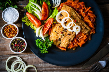 Fish dish - fried fish fillet on vegetable sauce on wooden table